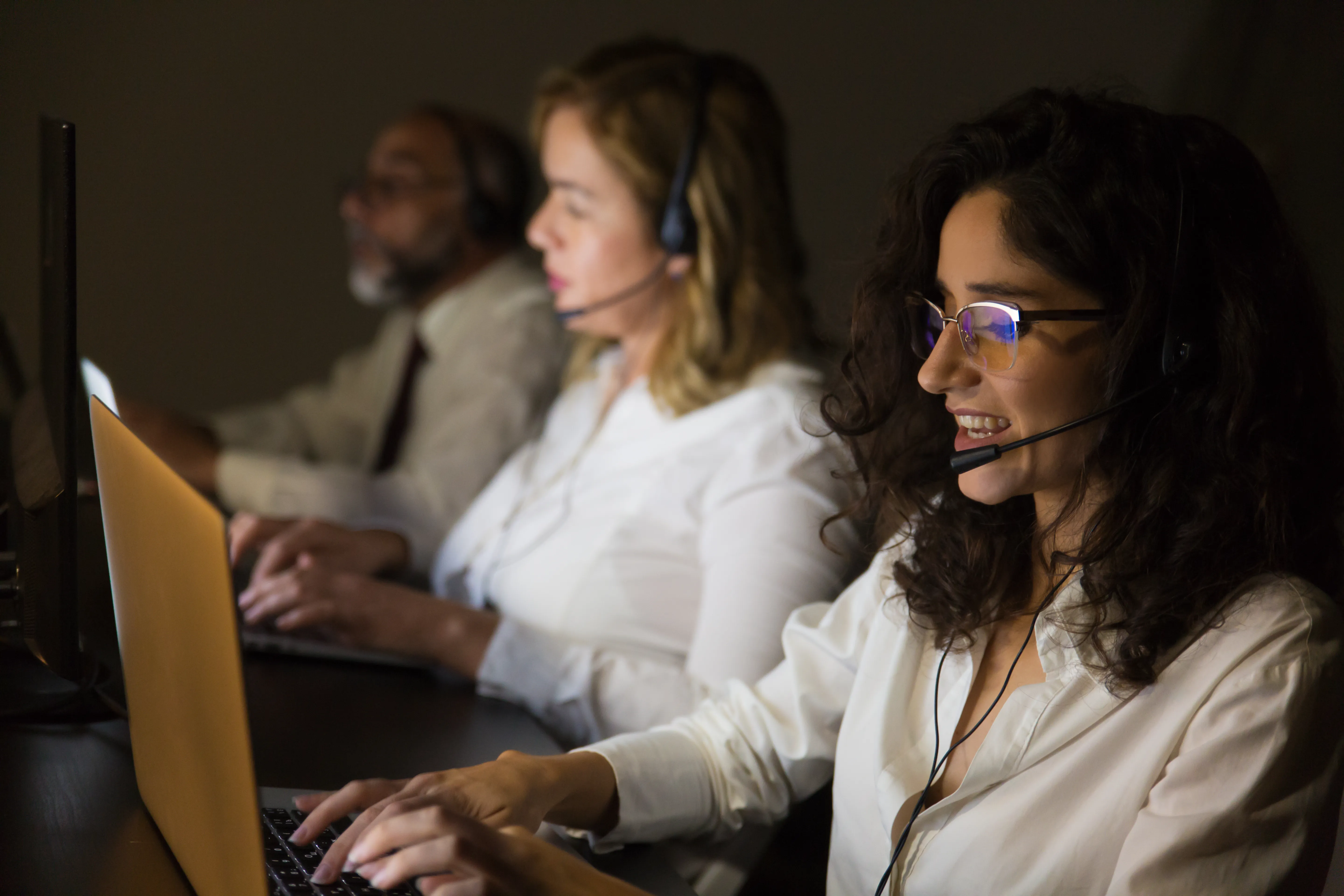 Funcionários com headsets atendendo clientes em uma central de suporte noturno, representando o atendimento eficiente que um sistema para cafeterias pode oferecer com suporte especializado.