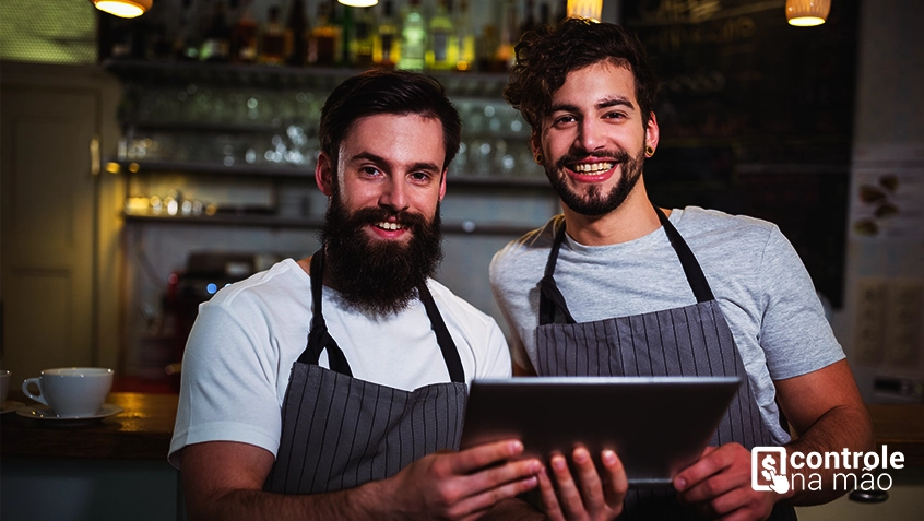 homens segurando tablet em frente a cozinha de restaurante - sistema para restaurantes controle na mao