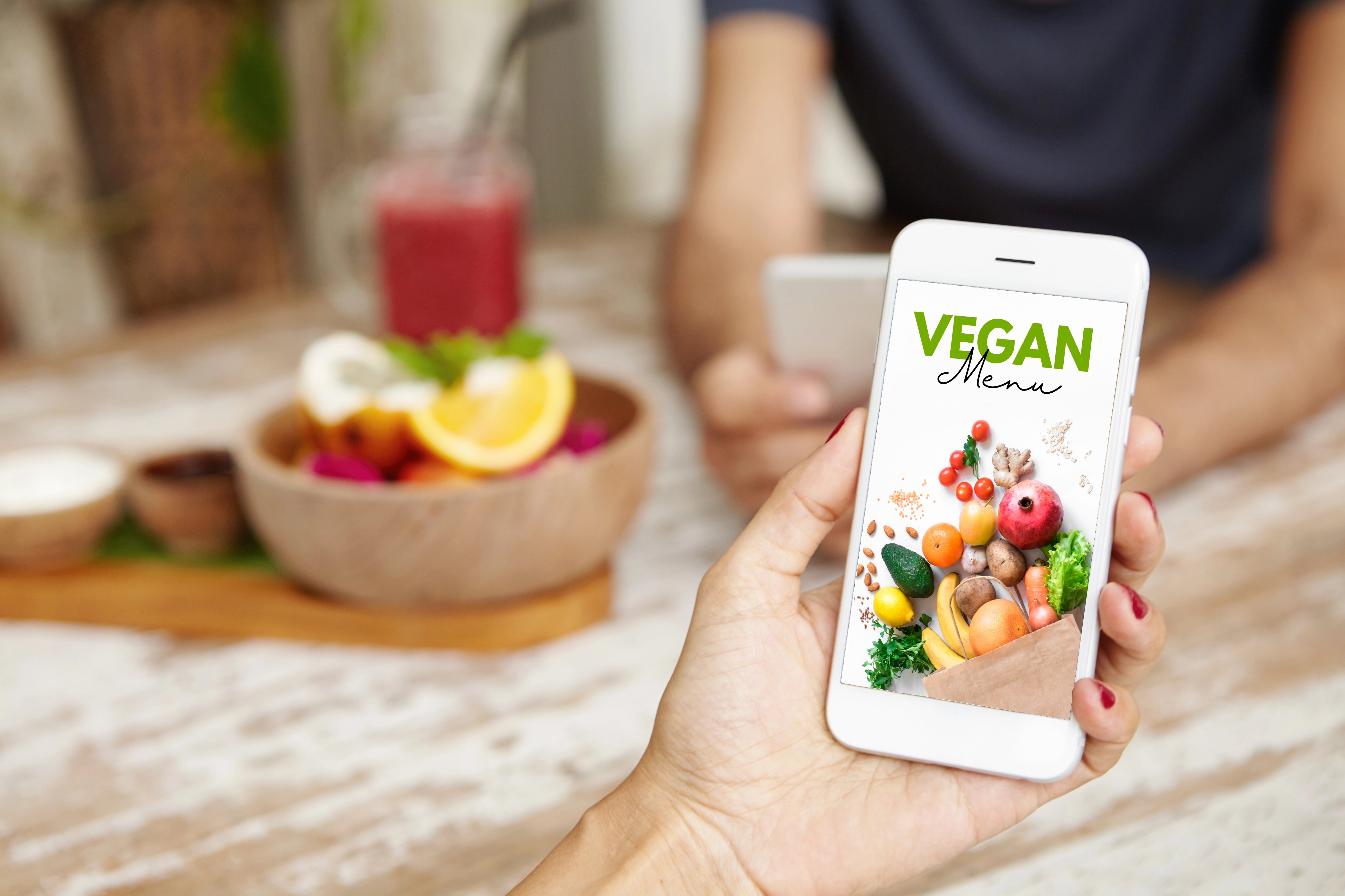 frutas e suco em cima de uma mesa com uma pessoa segurando o celular com um cardapio vetetariano aberto