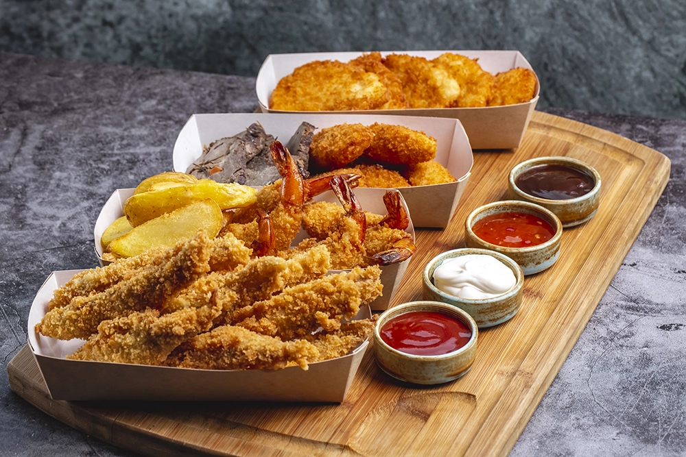 Quatro caixas de pepitas com queijo de camarão e peixe com molho de quatro em cima de uma mesa