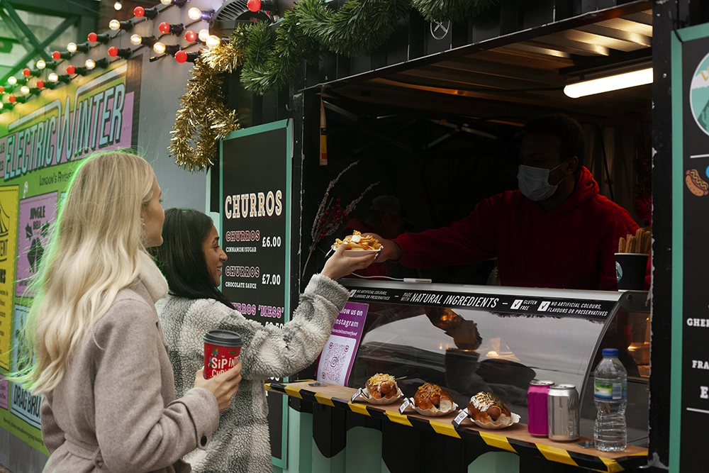 homem em seu food truck oferecendo seu produto a duas clientes