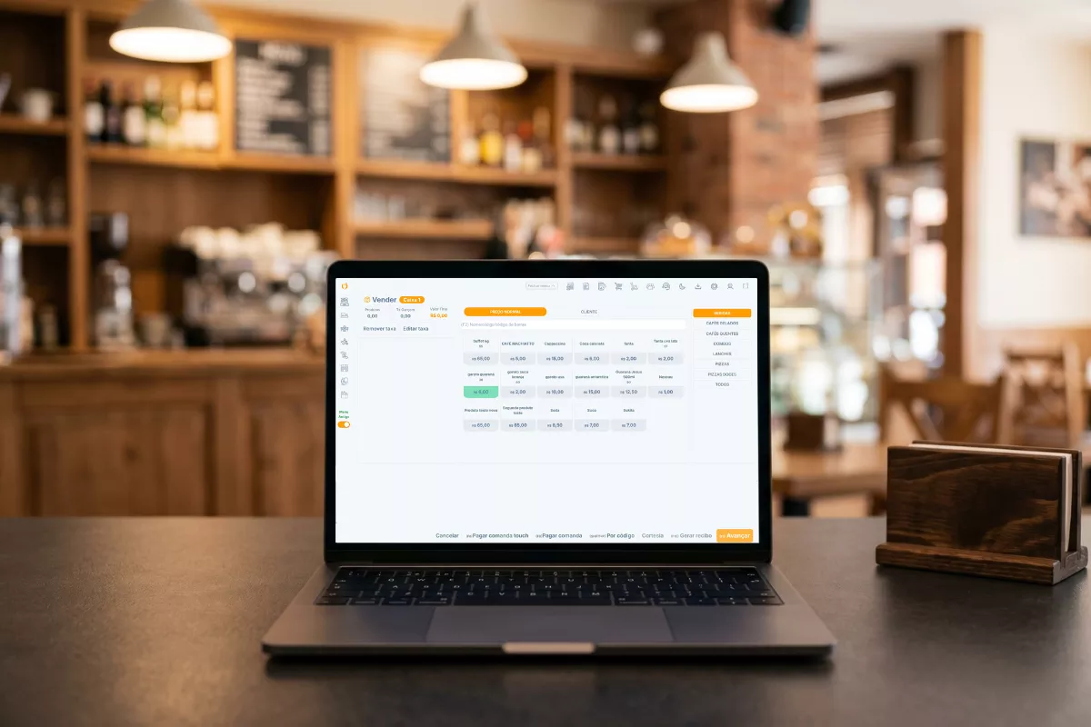 notebook aberto sobre mesa de madeira em cafeteria mostrando o sistema ControleNaMão na tela do PDV, com prateleiras e ambiente do restaurante ao fundo