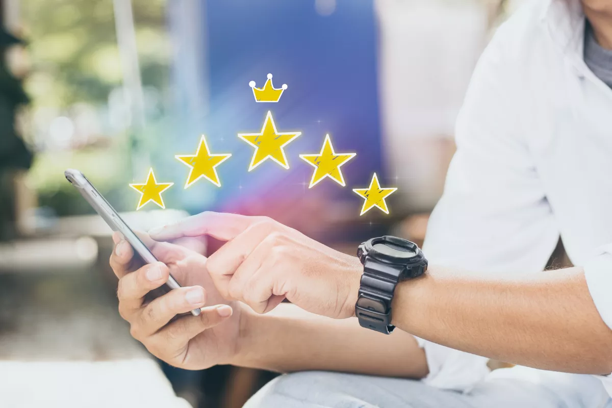 Mãos de pessoa segurando smartphone com ilustração de cinco estrelas douradas e coroa sobrepostas, representando avaliação positiva de restaurante