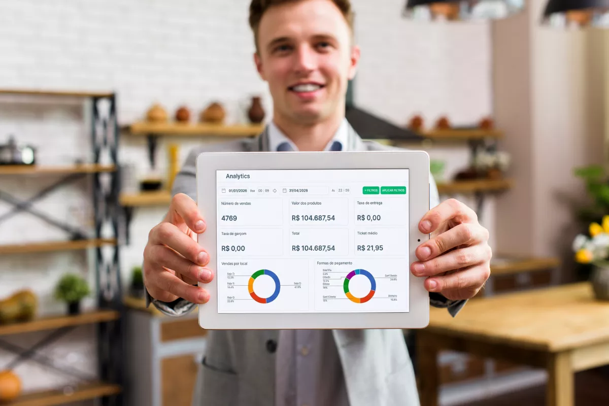 Dono de restaurante sorrindo e segurando tablet com dashboard do ControleNaMão mostrando número de vendas, faturamento e ticket médio