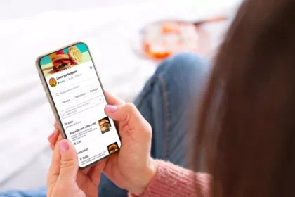 Cliente deitada no sofá em casa acessando cardápio digital de hamburgueria pelo celular, com categorias, fotos dos pratos e preços visíveis na tela