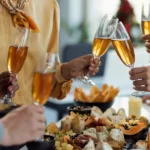 Grupo de pessoas brindando com taças de espumante sobre mesa farta com petiscos, frios e finger foods em celebração especial no restaurante