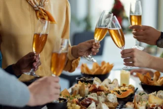 Grupo de pessoas brindando com taças de espumante sobre mesa farta com petiscos, frios e finger foods em celebração especial no restaurante