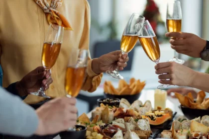 Grupo de pessoas brindando com taças de espumante sobre mesa farta com petiscos, frios e finger foods em celebração especial no restaurante
