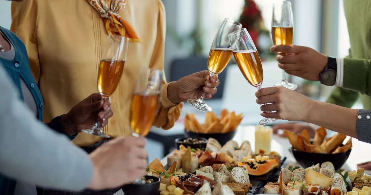 Grupo de pessoas brindando com taças de espumante sobre mesa farta com petiscos, frios e finger foods em celebração especial no restaurante