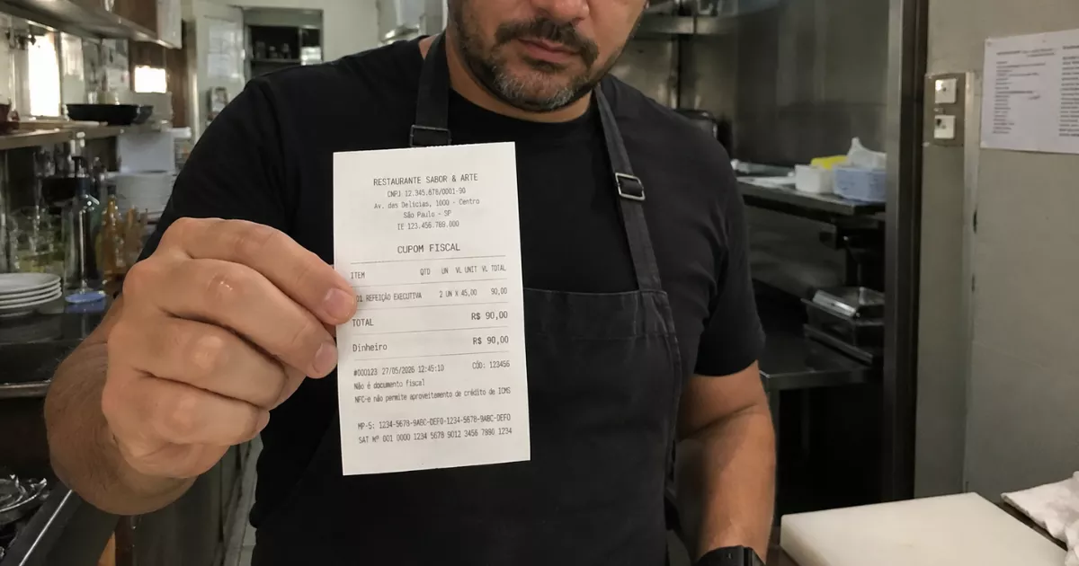 Funcionário de restaurante com avental cinza segurando cupom fiscal impresso em frente à cozinha, mostrando os dados da NFC-e emitida