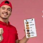 Entregador de uniforme vermelho segurando caixas de delivery empilhadas e prancheta com cardápio ilustrado de marmita, hambúrguer, pizza, açaí, comida japonesa e fitness