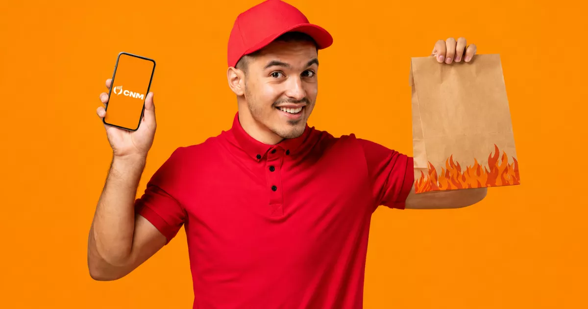 Entregador de camiseta e boné vermelhos segurando celular com o app ControleNaMão em uma mão e sacola de delivery na outra, em fundo laranja