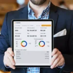 Gestor de terno segurando tablet que exibe o painel Analytics do ControleNaMão com gráficos de vendas por local e formas de pagamento