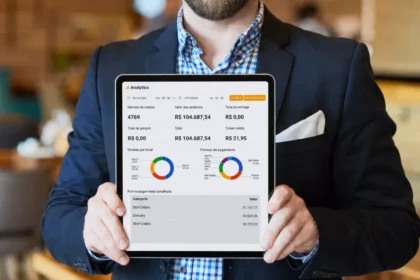 Gestor de terno segurando tablet que exibe o painel Analytics do ControleNaMão com gráficos de vendas por local e formas de pagamento