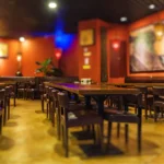 Salão de lanchonete com mesas e cadeiras de madeira, paredes coloridas e quadros decorativos, mostrando o ambiente de um estabelecimento de food service antes de abrir para o público