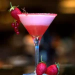 Cosmopolitan rosa em taça de martini com borda de açúcar, espuma no topo e guarnição de morango e groselha vermelha, fundo de bar desfocado