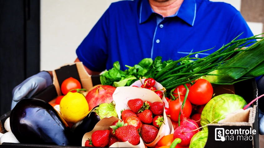 Entregador de compras com caixa cheia de frutas, verduras e legumes - Blog ControleNaMão