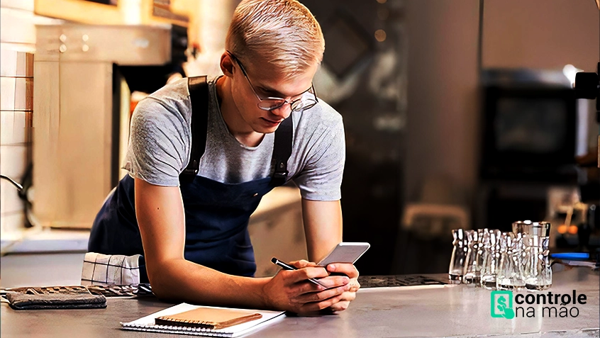 atendente de restaurante segurando celular, debruçado sobre bancada. sistema para restaurantes controle na mão