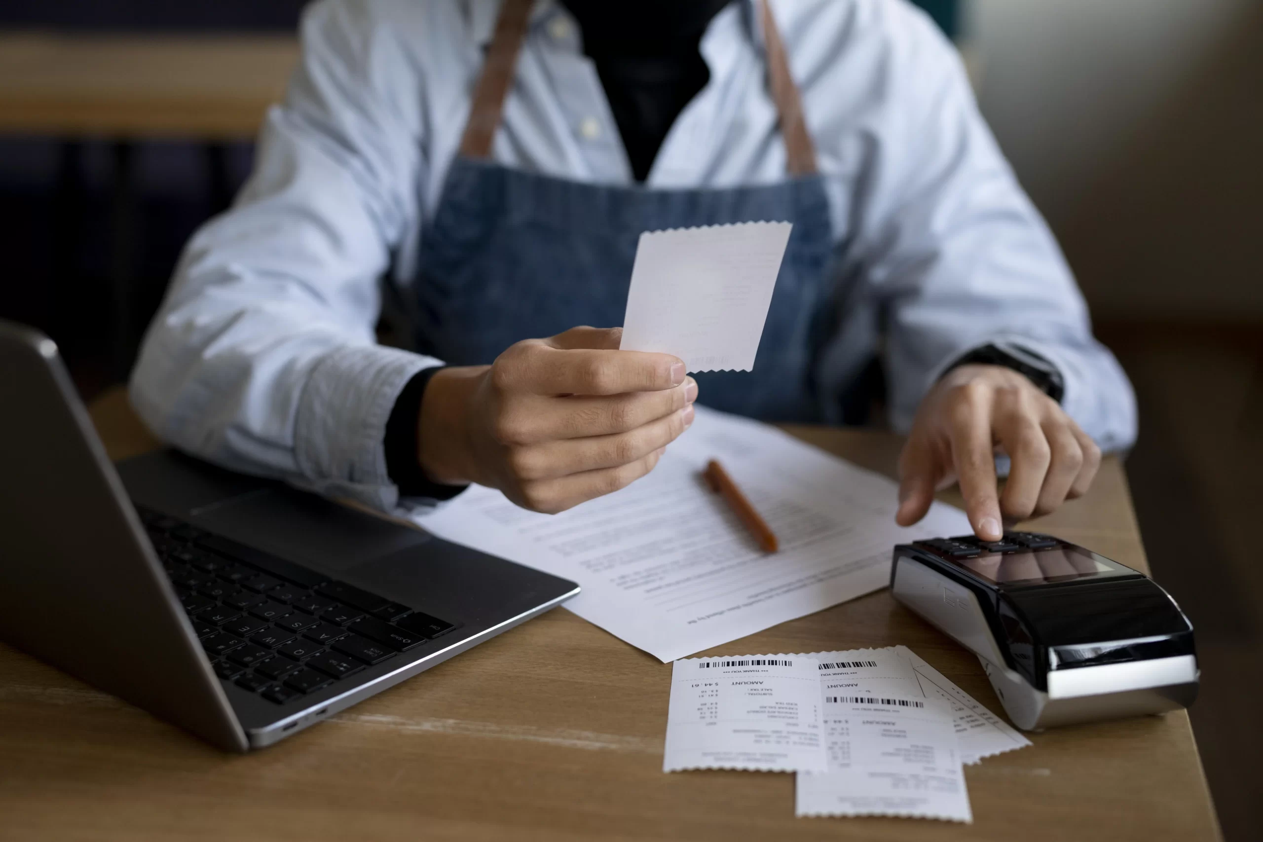 Dono de restaurante usando uma calculadora, rodeado por papéis, calculando como exatamente reduzir os custos em seu restaurante