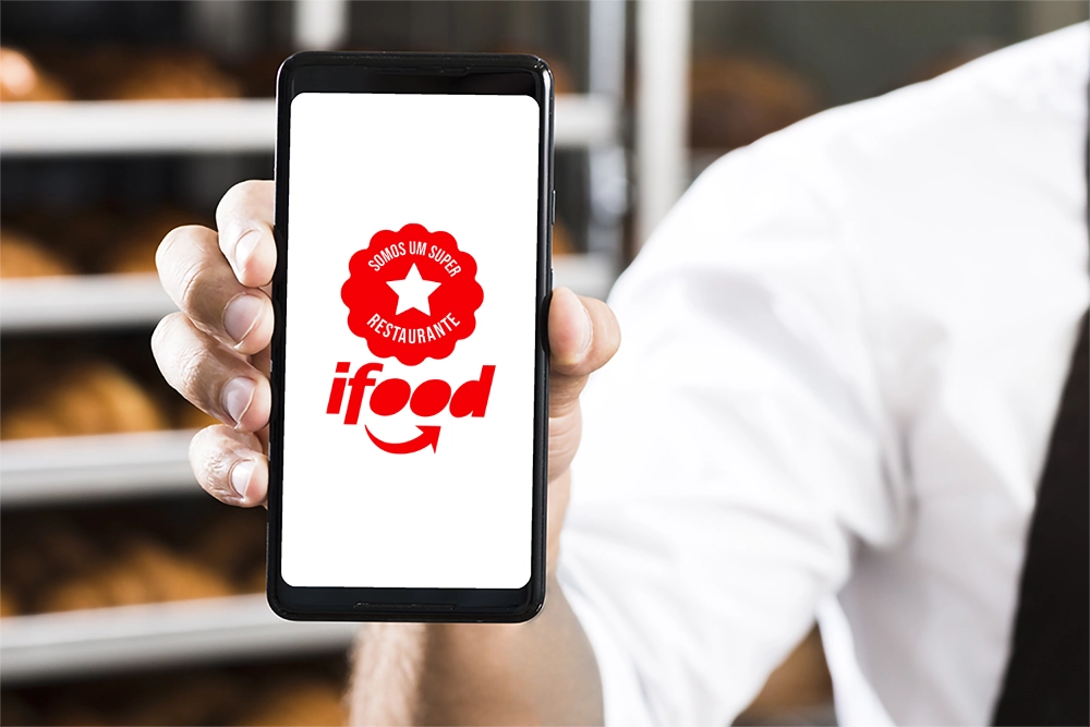 Dono de restaurante segurando um celular para câmera com o Selo Super Restaurante iFood