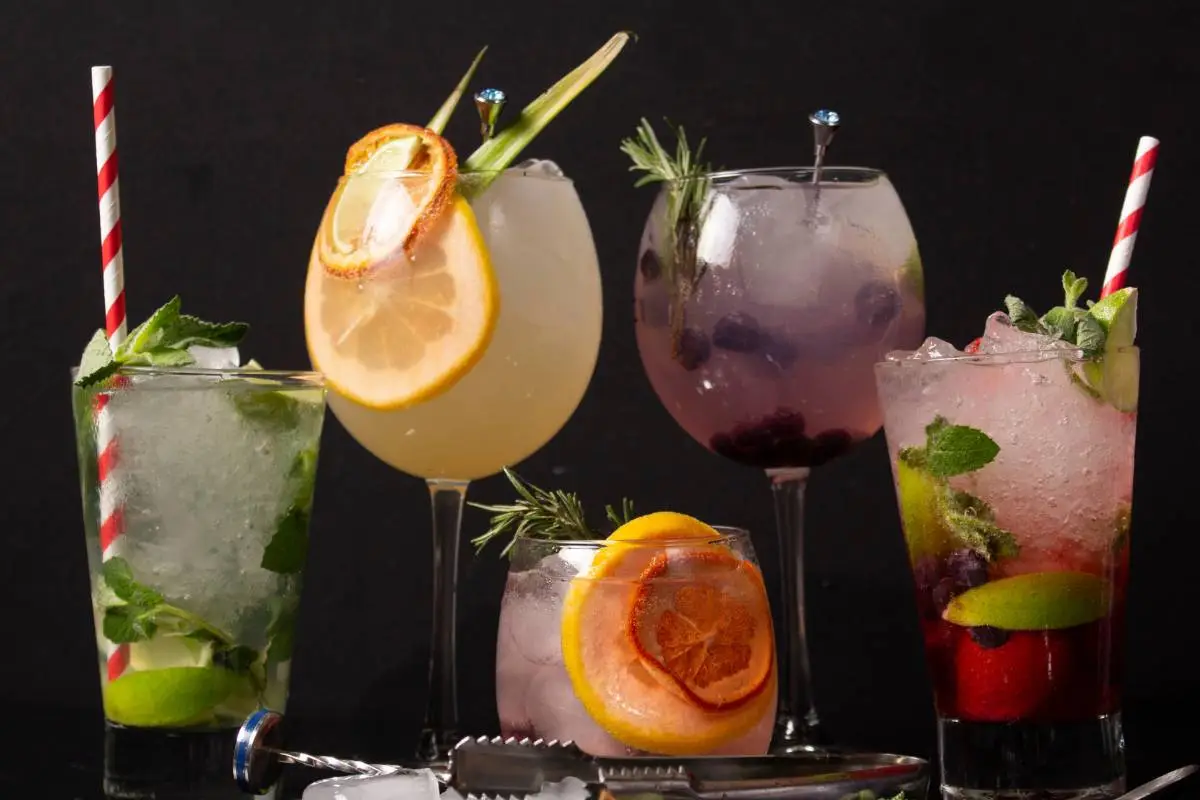 Drinks artesanais variados com frutas frescas e gelo servidos em copos altos.