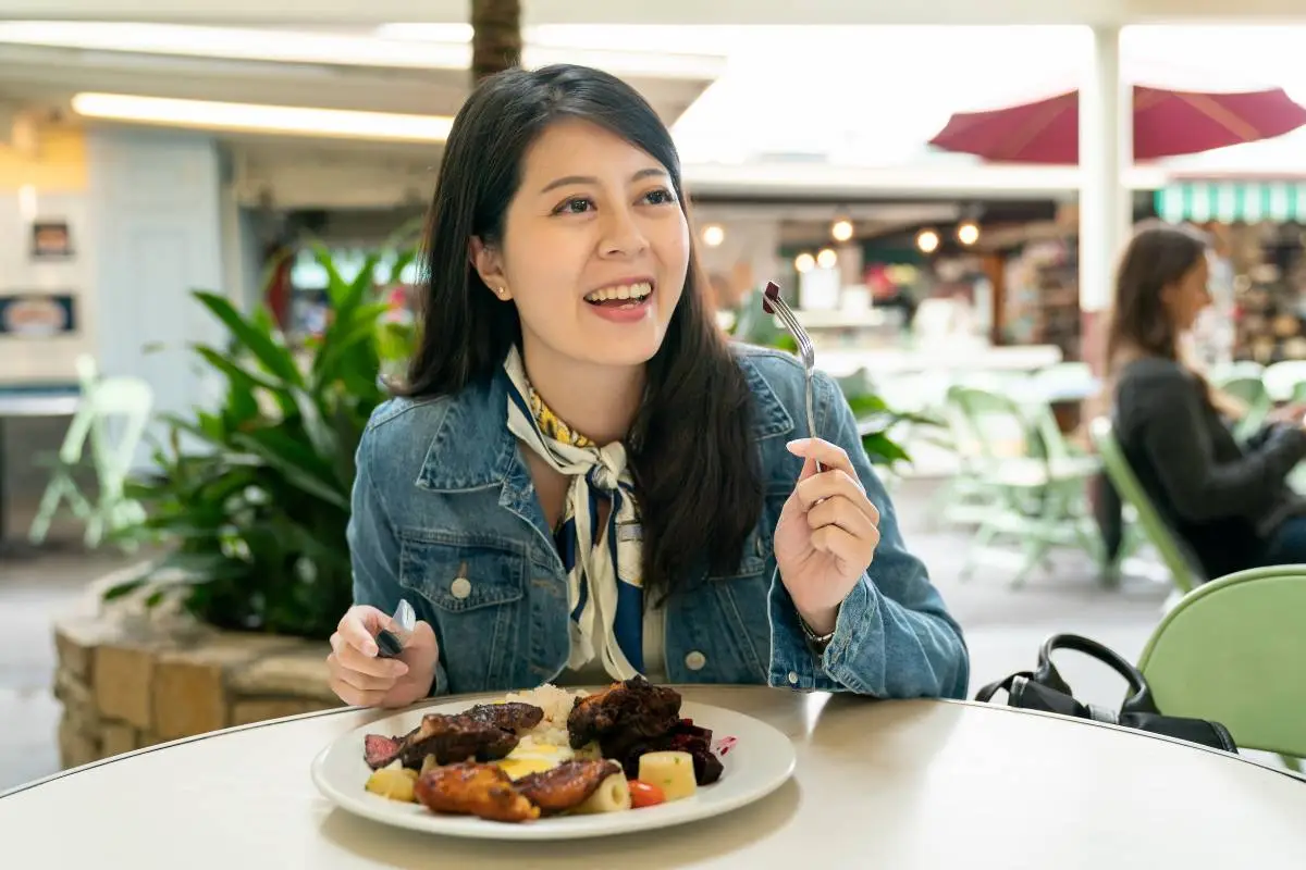 Mulher sorridente comendo em um restaurante, transmitindo a ideia de uma refeição prazerosa e ambiente acolhedor.