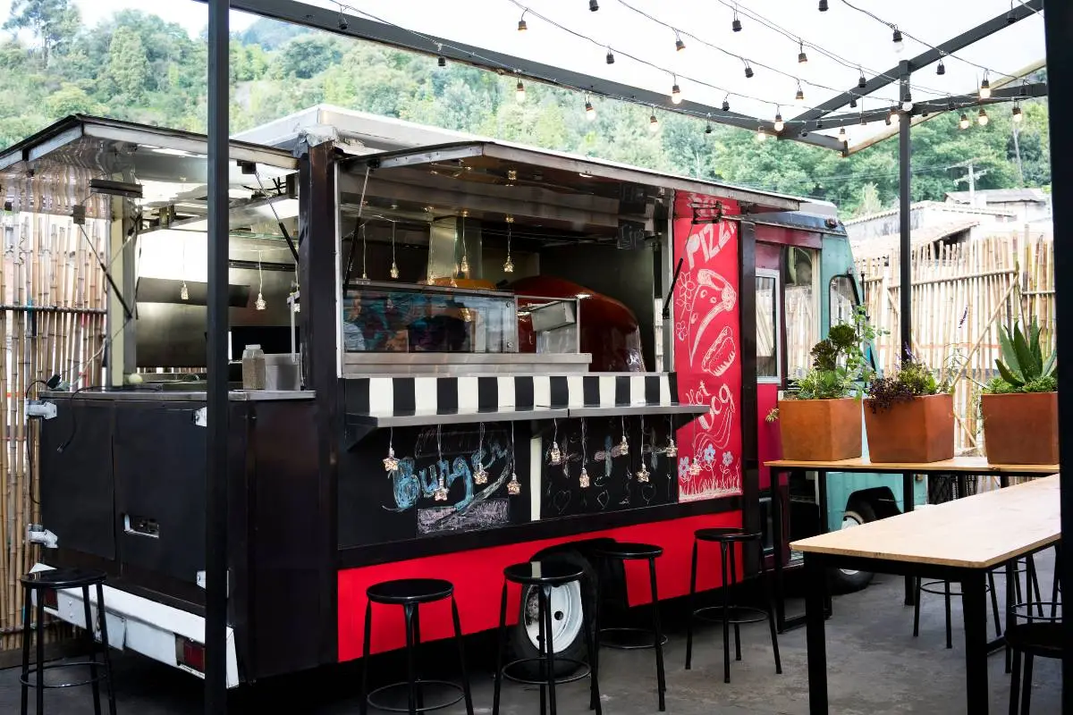 Atendente de food truck sorrindo enquanto entrega hambúrgueres frescos para um cliente, exemplificando o atendimento personalizado e a experiência gastronômica dos food trucks