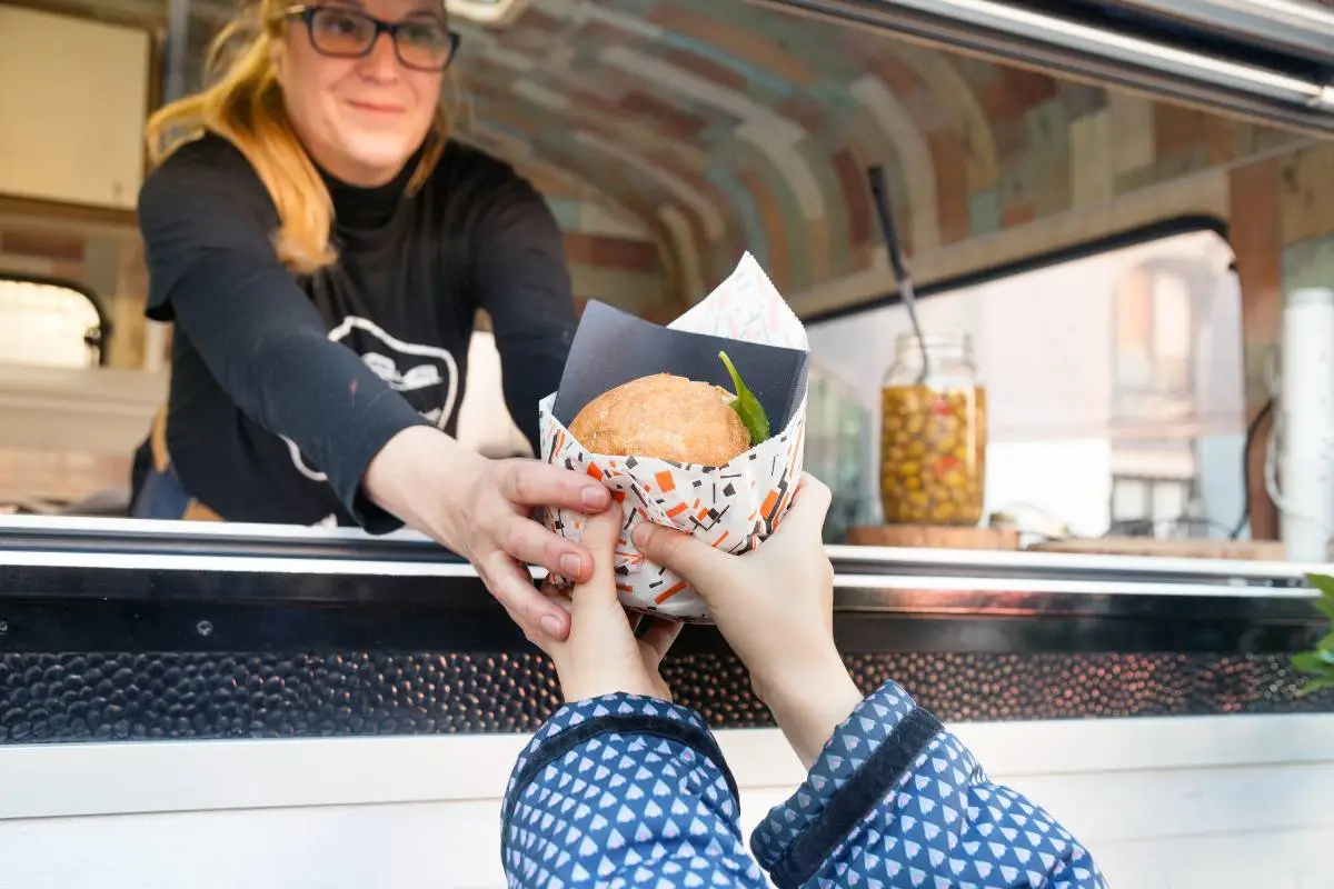 Cliente recebendo um lanche em um food truck de uma atendente sorridente, ilustrando a interação e conveniência do modelo de negócio de food trucks