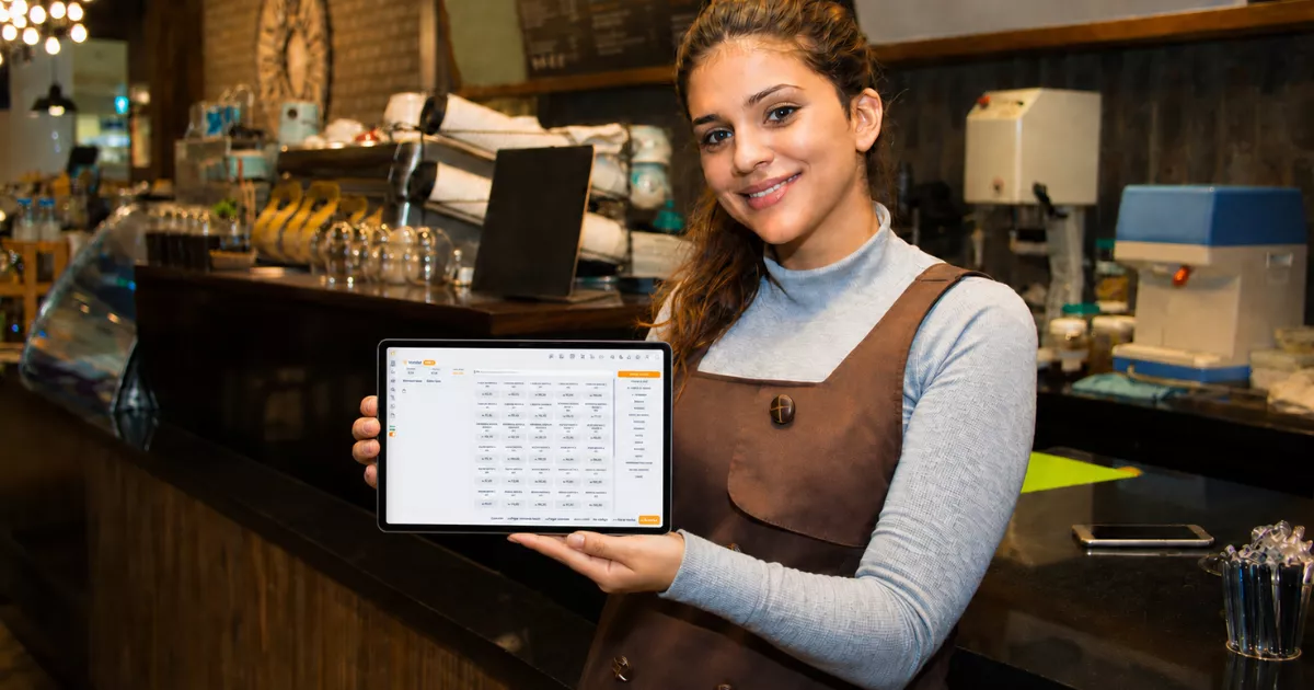 Gestora sorridente apresenta tablet com o sistema ControleNaMão aberto, em frente ao balcão de um restaurante durante a operação.