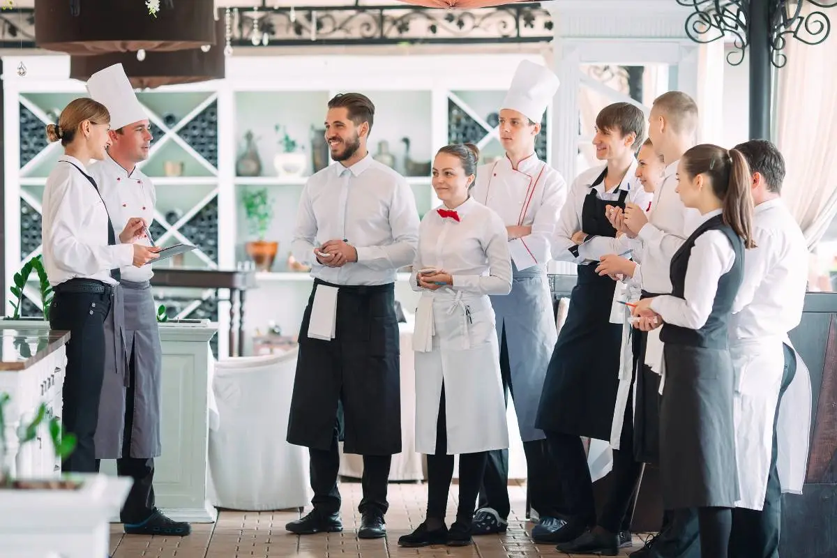 Equipe de restaurante em reunião, recebendo instruções de um chef e consultor, com foco em melhorar o atendimento e a operação.