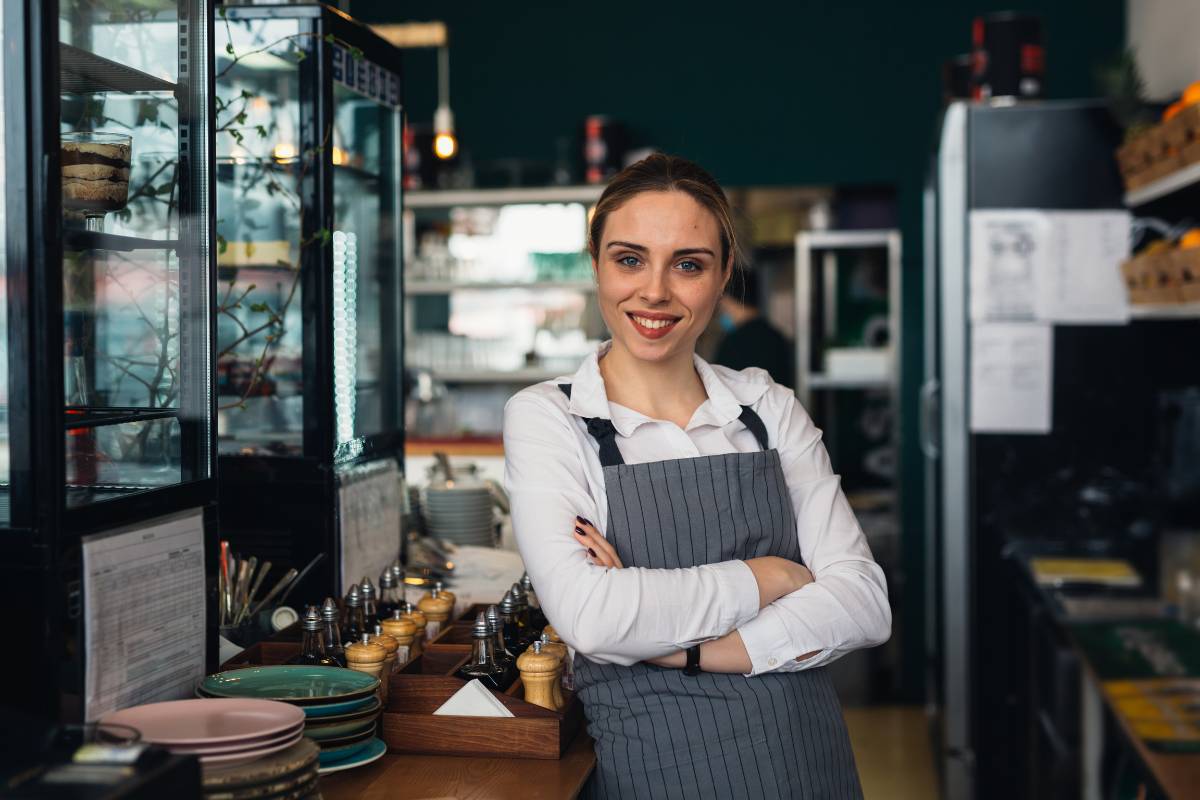 Mulher sorridente vestindo avental em uma lanchonete, demonstrando confiança e satisfação com o ambiente de trabalho