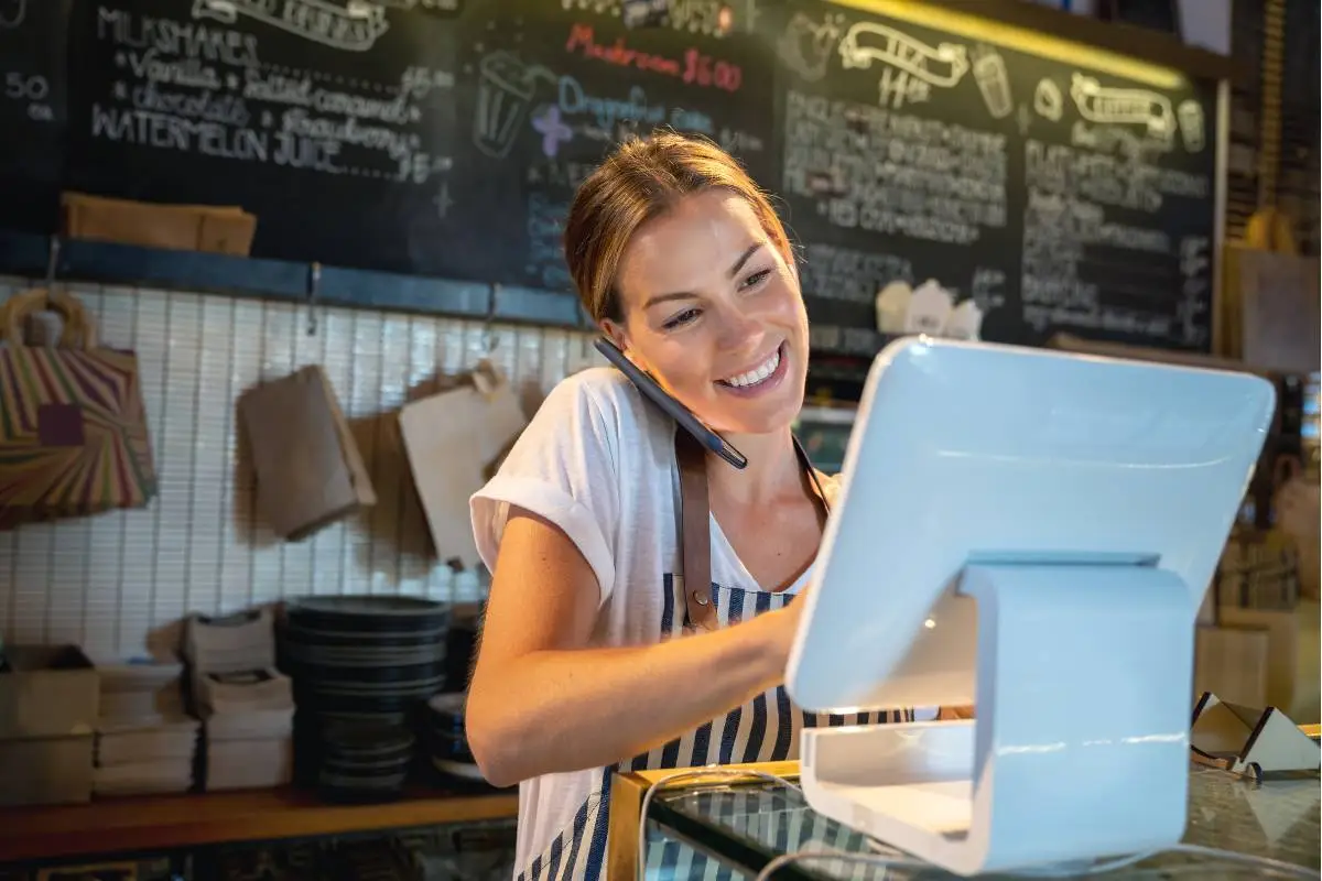 Funcionária de restaurante utilizando um sistema de pedidos online enquanto fala ao telefone, gerenciando o atendimento de forma eficiente.