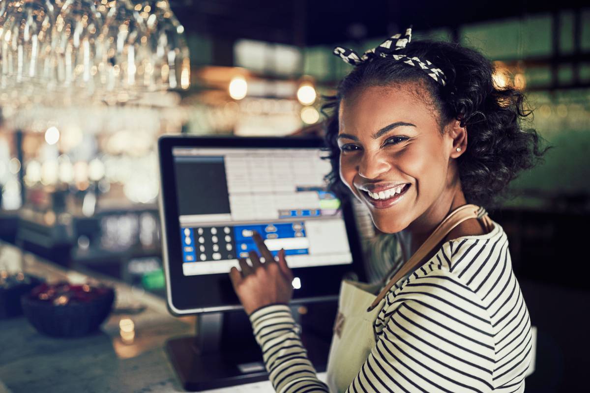 Mulher sorridente utilizando sistema de gestão em tela sensível ao toque em restaurante.