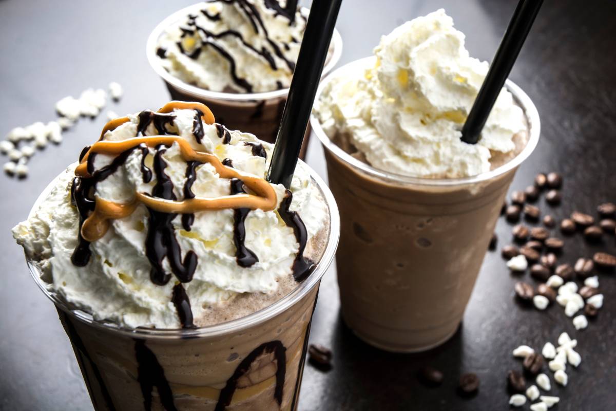 Frappuccinos com chantilly, cobertura de chocolate e caramelo, acompanhados de grãos de café