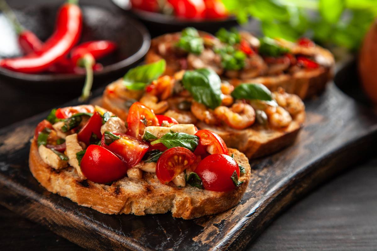 Bruschettas com pão italiano tostado, cobertas com tomate, manjericão e queijo, servidas em tábua rústica.