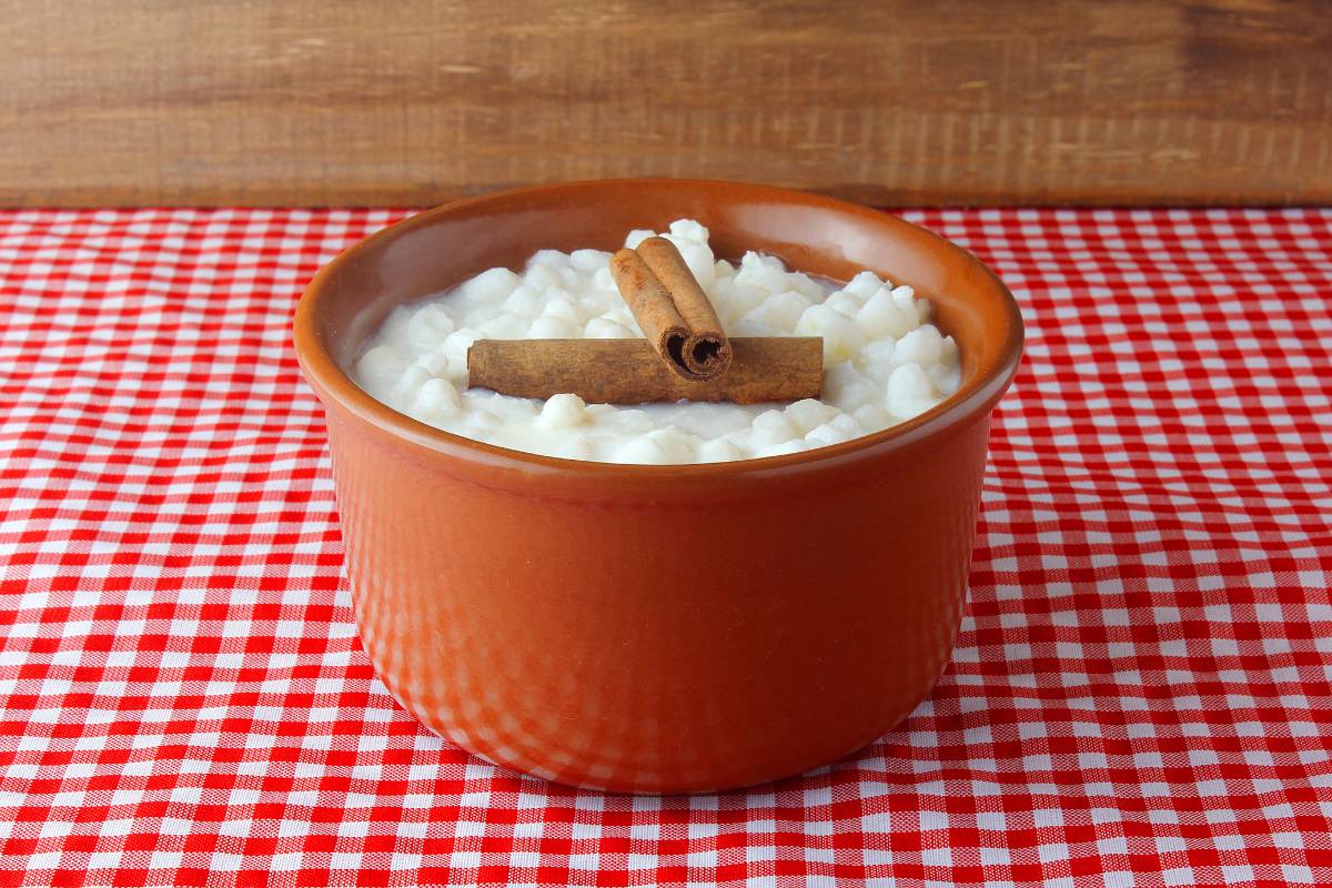 Canjica (Mungunzá) doce com canela - Sobremesa brasileira feita com milho branco cozido, leite de coco, açúcar e cravo, decorada com pau de canela em uma tigela de barro.