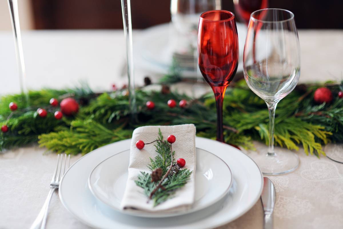 Mesa de jantar preparada para o Natal, com guardanapo decorado com galhos verdes e copos vermelhos, proporcionando um toque sofisticado e natalino.