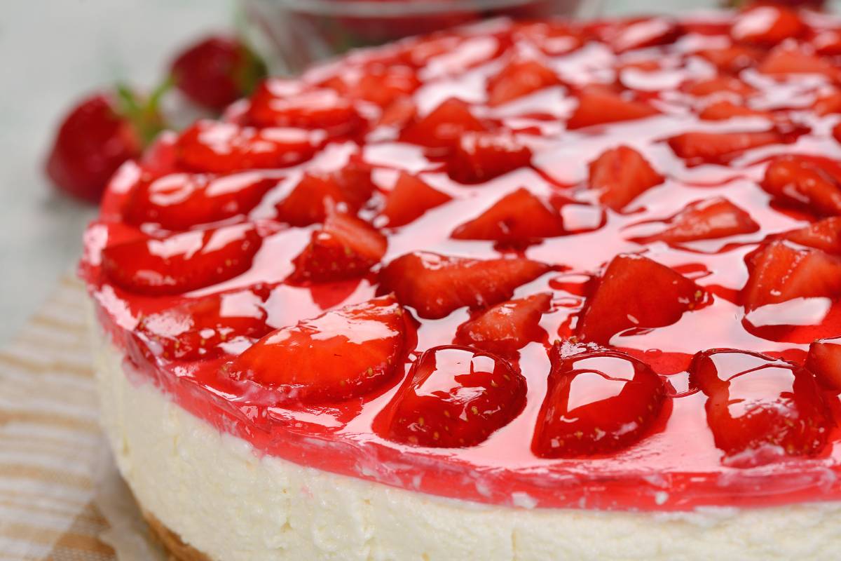 Cheesecake decorado com calda e pedaços de morango, em close detalhado.