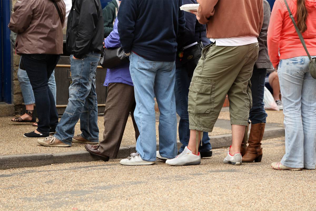 Pessoas esperando em fila ao ar livre, possivelmente aguardando para entrar em um restaurante.