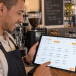 Proprietário de cafeteria usa o PDV desktop do ControleNaMão em um tablet no balcão, com máquina de café e vitrine ao fundo.
