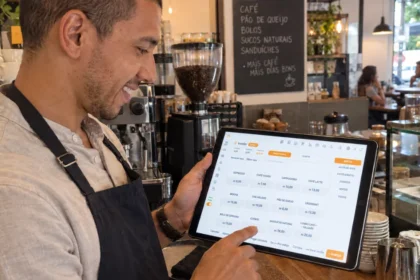 Proprietário de cafeteria usa o PDV desktop do ControleNaMão em um tablet no balcão, com máquina de café e vitrine ao fundo.