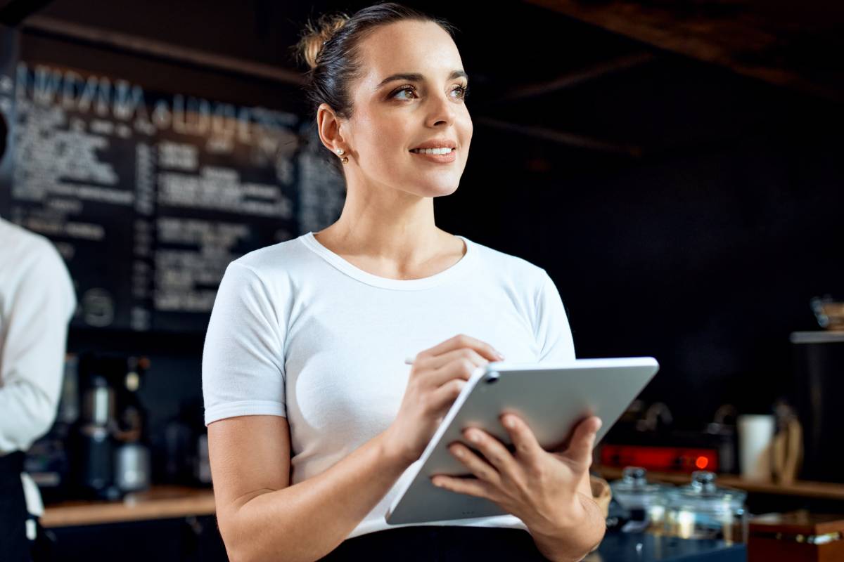 Garçonete usando tablet para anotar pedidos em restaurante, destacando a importância de tecnologia para gestão de pedidos