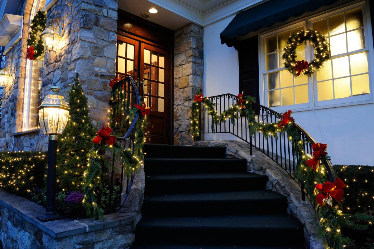 Entrada de restaurante decorada com guirlandas iluminadas e laços vermelhos ao longo do corrimão, criando uma recepção festiva e convidativa para os clientes.