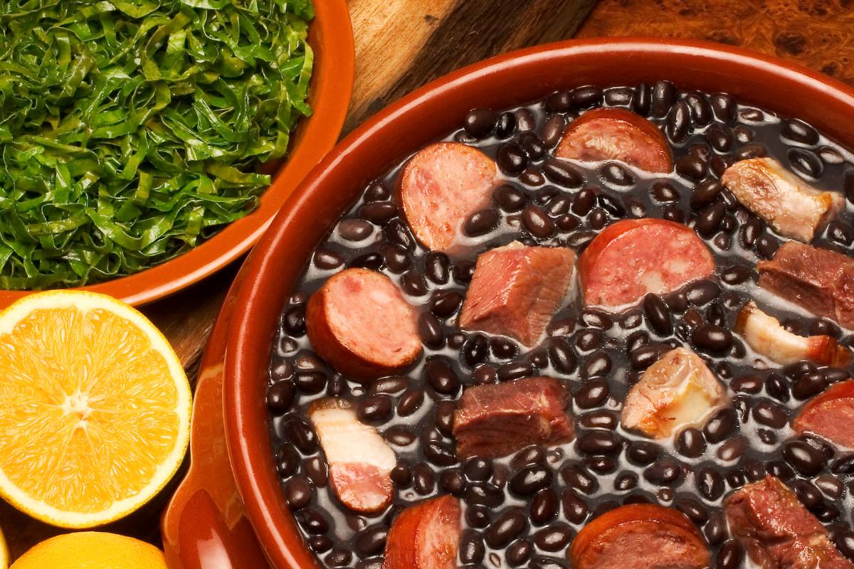 Feijoada brasileira com acompanhamentos - Feijão preto cozido com carnes suínas, servido com couve refogada e laranja fatiada em pratos de barro.