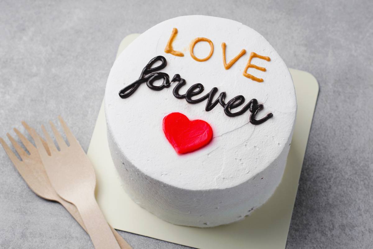 Bentô Cake branco decorado com a frase 'Love forever' e um coração vermelho, acompanhado de garfos de madeira ao lado