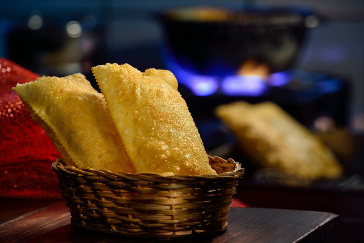 Cesta com pastéis dourados e crocantes ao fundo, com ambiente rústico e fogão em chamas criando uma atmosfera acolhedora.