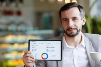 Gestor em cafeteria segura um tablet com relatório de vendas enquanto toma café.