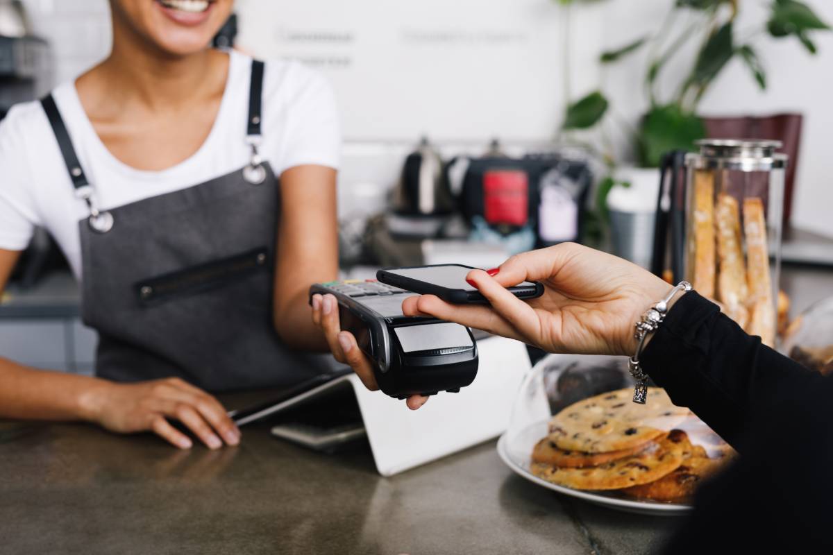 Cliente realizando pagamento por aproximação em um restaurante enquanto a atendente sorri.