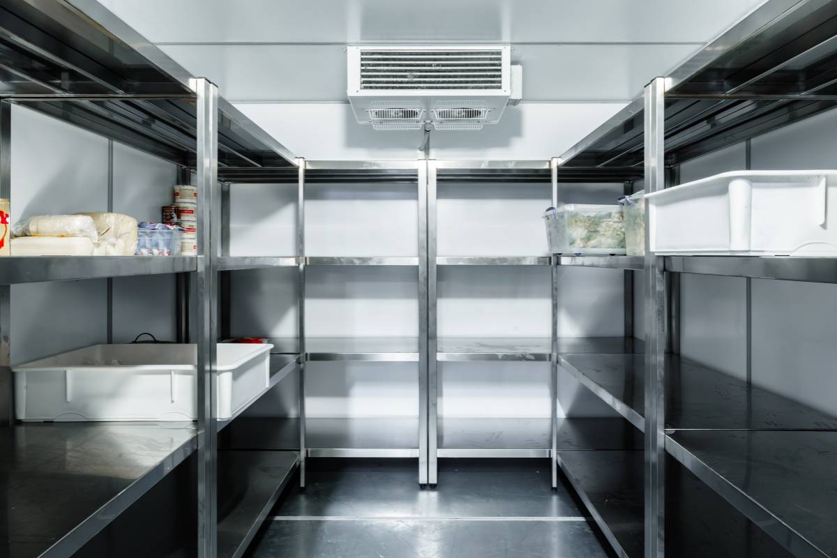 Prateleiras organizadas de um estoque refrigerado em restaurante, com poucos itens armazenados, destacando a importância do controle e organização de insumos perecíveis.