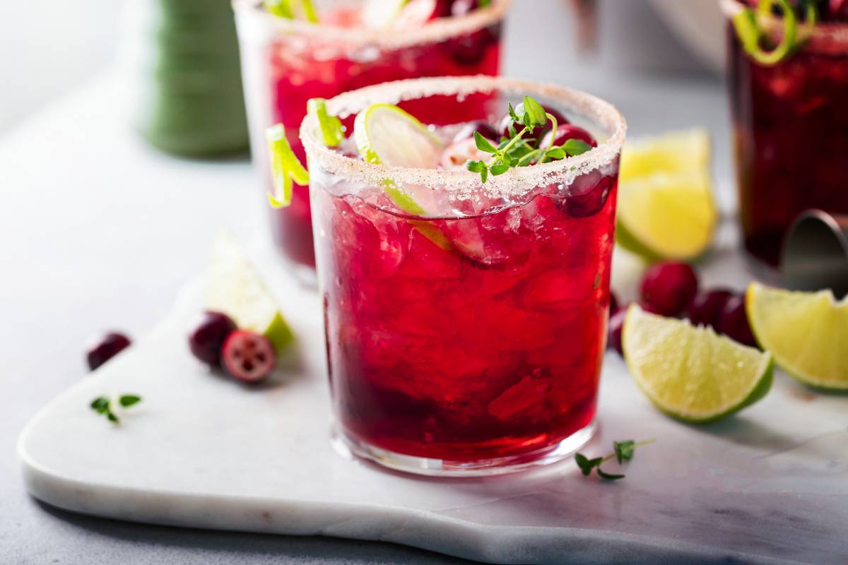 Mocktail vermelho decorado com limão, frutas vermelhas e borda de açúcar, servido em copo transparente com gelo.